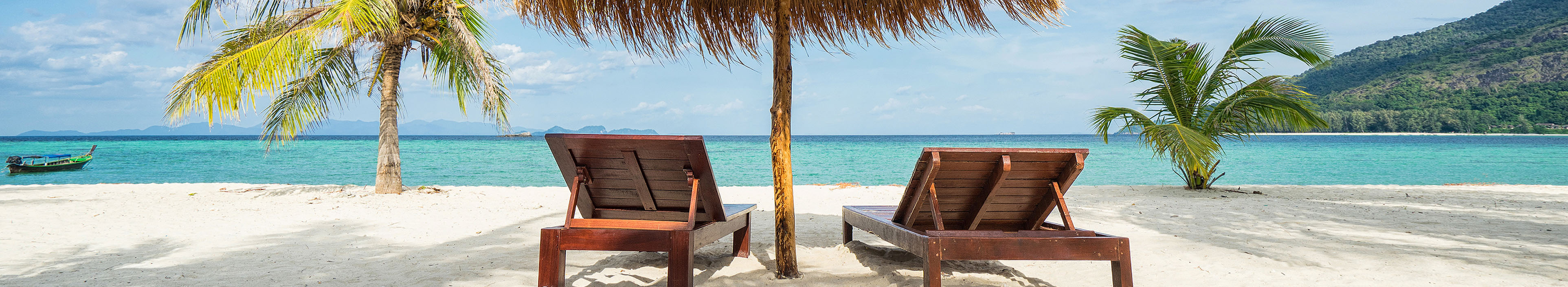 Liegestühle und ein Sonnenschirm an einem tropischem Strand