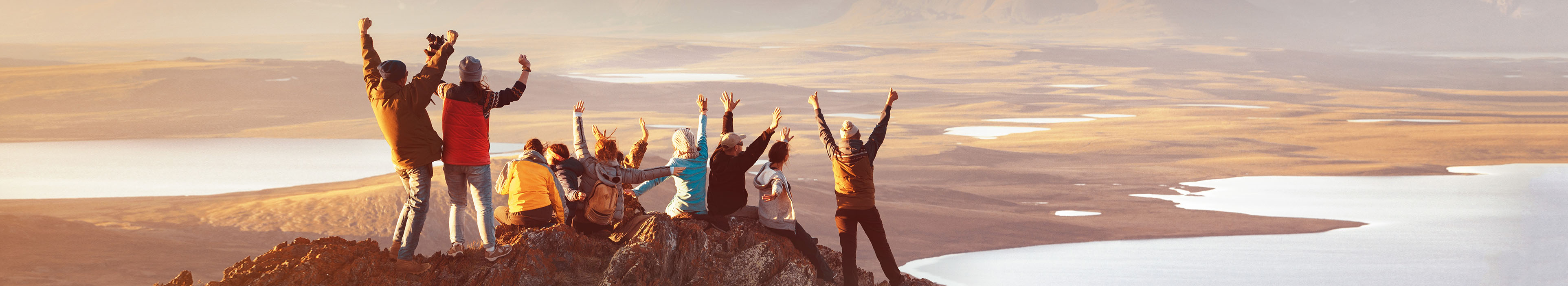 Reisegruppe steht auf dem Berg und genießt den Ausblick mit Sonnenaufgang. Alle haben ihre Hände gehoben und jubeln.