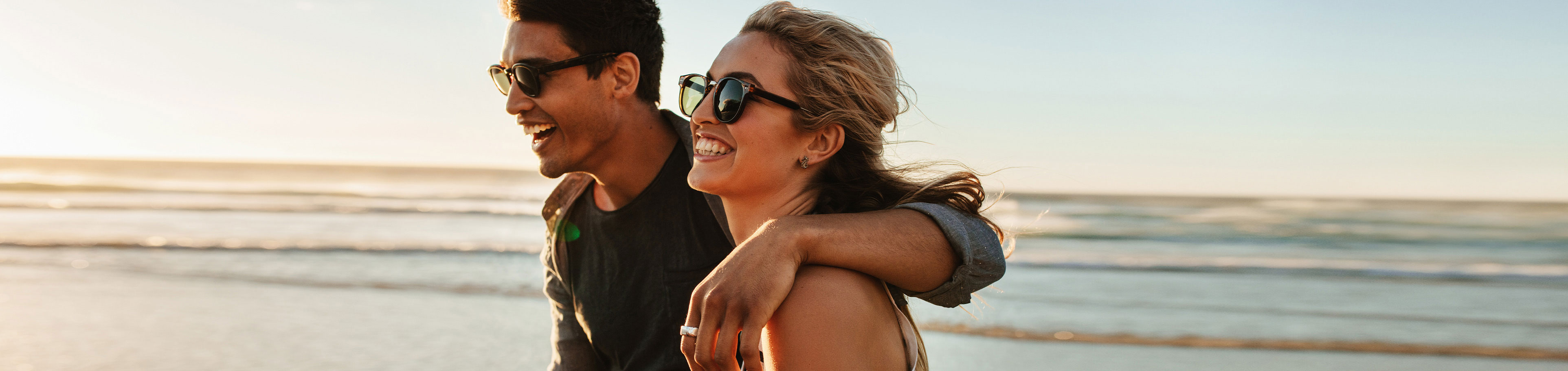 Fröhliches Paar mit Sonnenbrille am Strand 