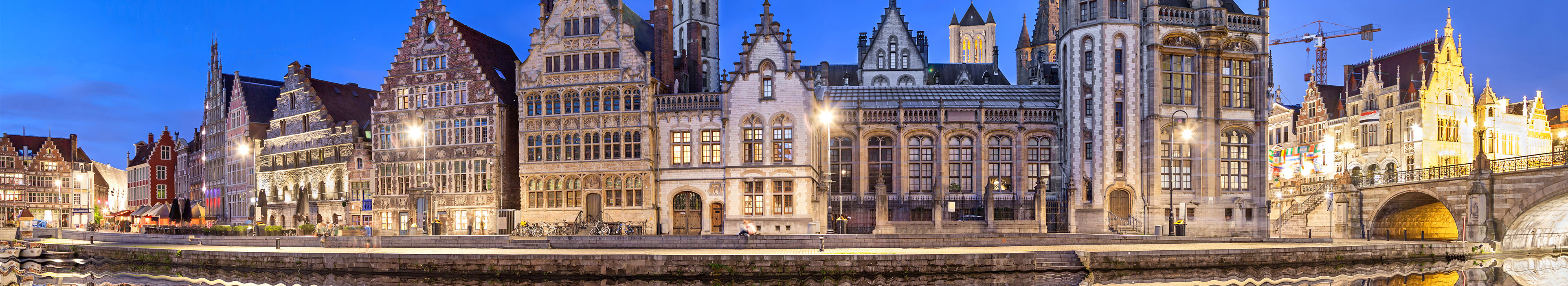 Die Skyline der Stadt Gent in Belgien spiegelt sich bei Nacht in einem Fluss.