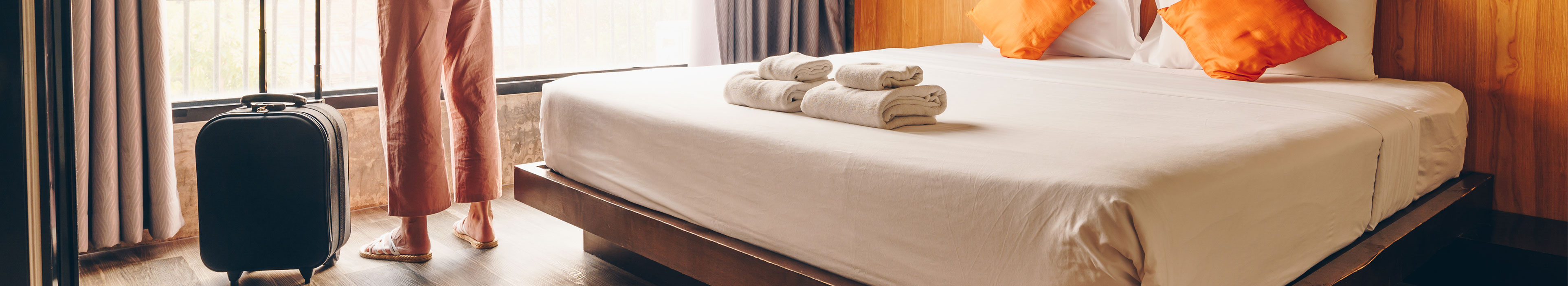 Eine Frau steht in einem Hotelzimmer mit ihrem Koffer und schaut aus dem Fenster.