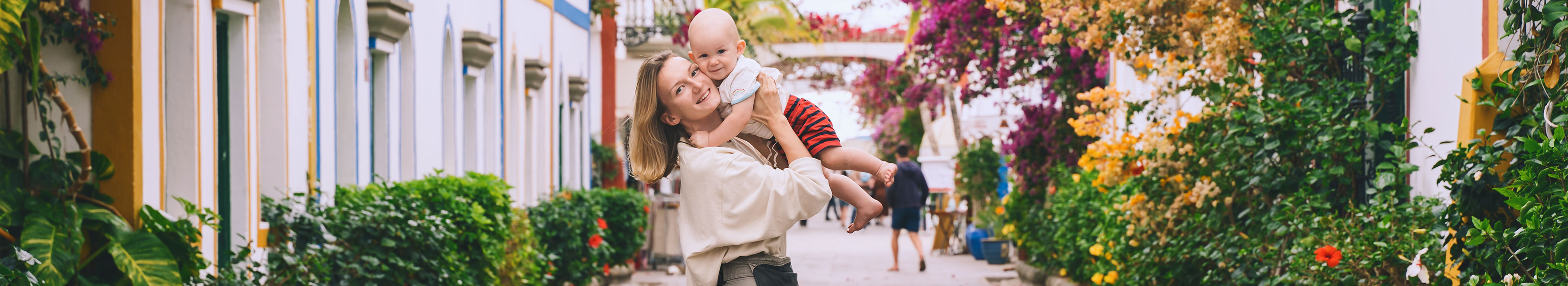 Mutter und Baby auf einer schönen Straße voller blühender Bäume in Puerto Mogan, Gran Canaria, Spanien