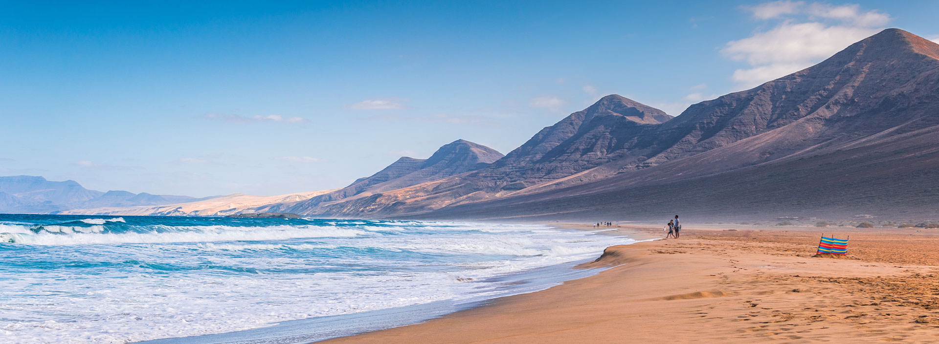 Urlaub Gran Canaria. Meer mit hohen Wellen und Menschen die am langen weitläufigen Strand laufen.