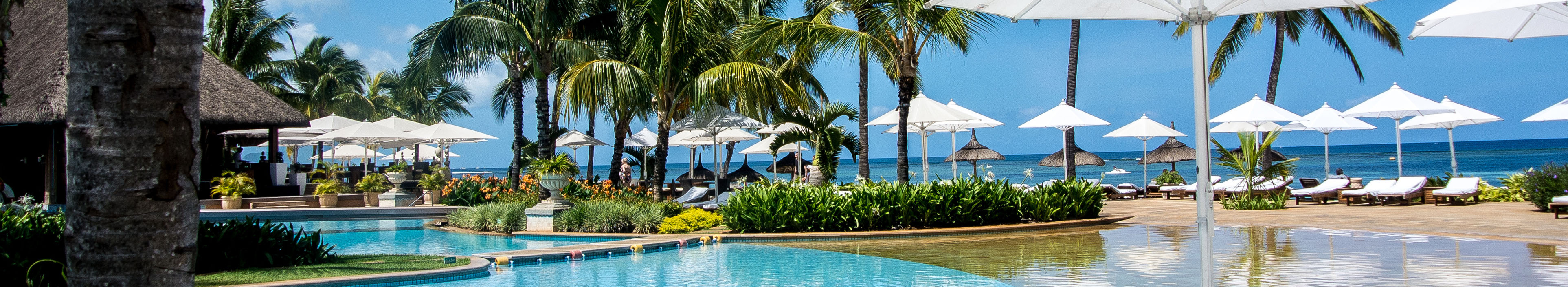 Hotel auf Mauritius, Pool, Palmen, Liegen und Sonnenschirme, im Hintergrund das Meer. 