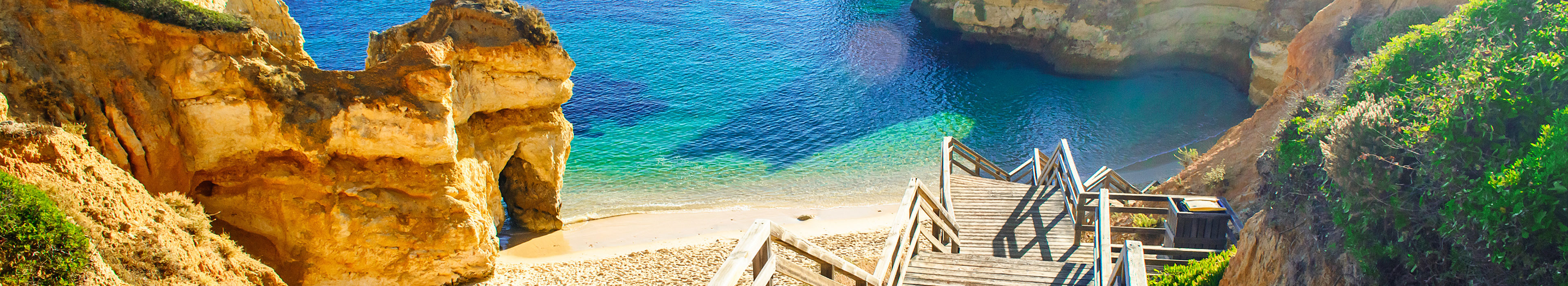 Urlaub Portugal. Holzsteg der runter zum Strandabschnitt führt. Hellbraune Felsen drumherum und im Meer.