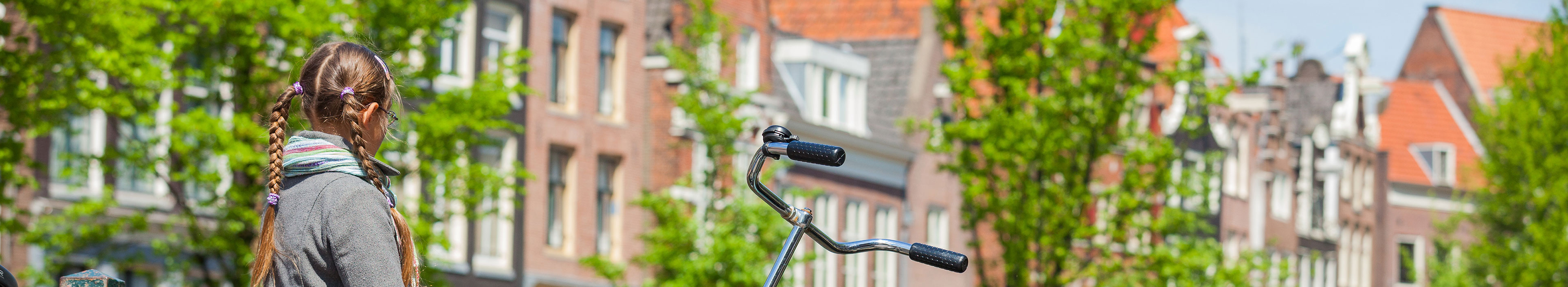Ein Mädchen steht in Amsterdam auf einer Brücke, neben ihr ein Fahrrad, im Hintergrund Häuser. 