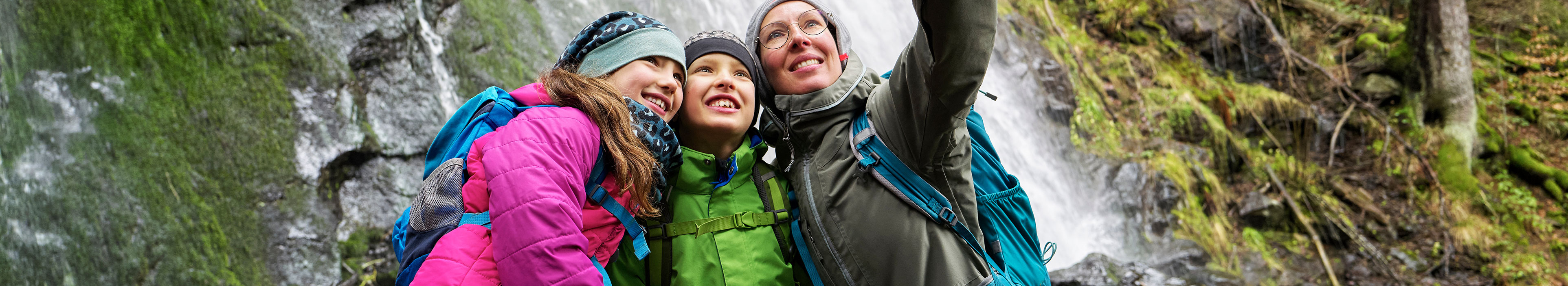 Eine Familie im Schwarzwald macht vor einem Wasserfall ein Selfie.